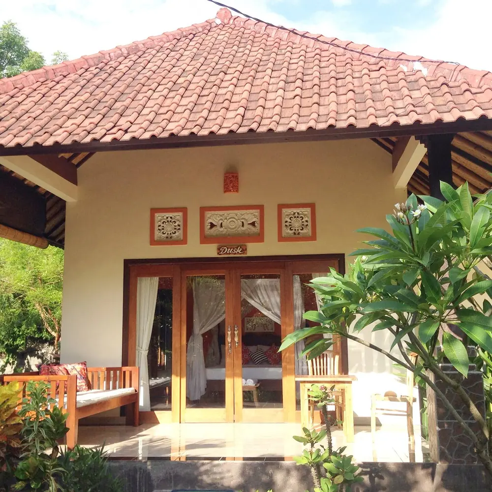 A Kirana bungalow with a tiled roof among frangipani and garden plants