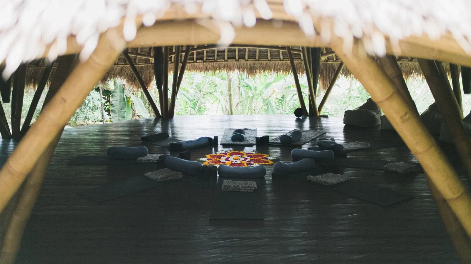 An open bamboo pavilion with yoga mats and cushions